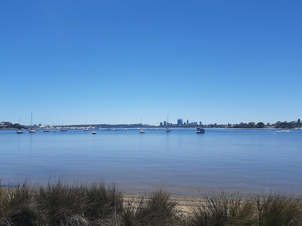 The mouth of the Canning River in Perth, Western Australia, with moored yachts and the city skyline in the distance
